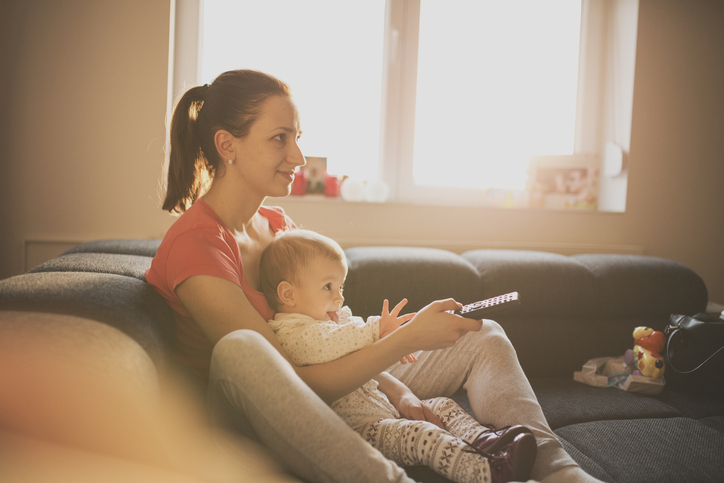 Young woman sitting on the bed holding baby and remote controler